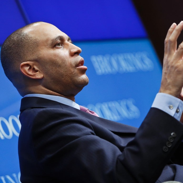 Hakeem Jeffries in front of a blue wall with his hand and arm raised