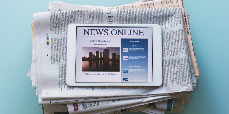 Photo of a stack of newspapers and an iPad displaying - News Online