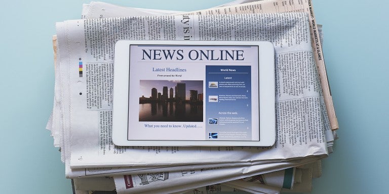 Photo of a stack of newspapers and an iPad displaying - News Online