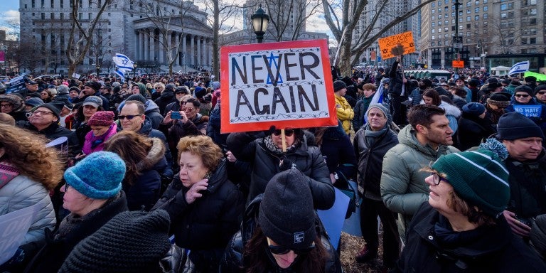 Photo of a crowd and a woman holding a sign saying "Never Again"