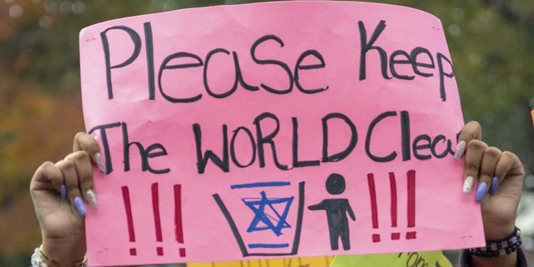 Sign at protest - "Please keep the world clean" with a photo of a person throwing away the Jewish star