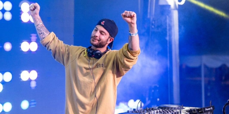 Israeli DJ Daniel Vaknin, in a yellow sweater stands with his arms raised, expressing joy or celebration. 
