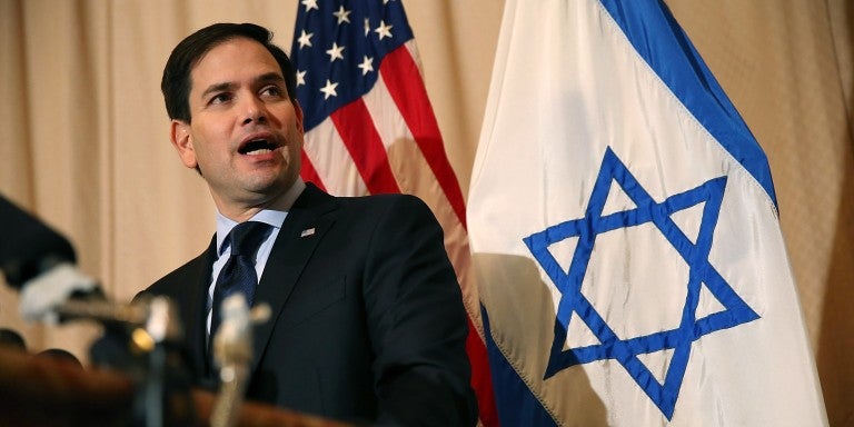 U.S. Sen. Marco Rubio (R-FL) speaks into a microphone, in front of U.S. and Israeli flags