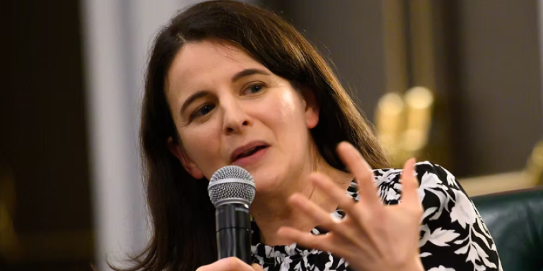 Author Sarah Hurwitz, wearing a black and white patterned dress, holding a microphone, speaking and gesticulating