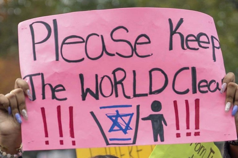 Sign at protest - "Please keep the world clean" with a photo of a person throwing away the Jewish star