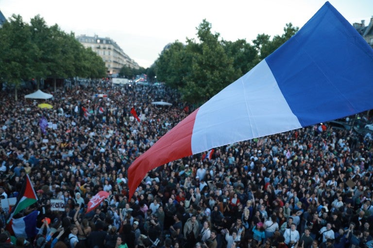 Large french flag waving outside in front of a crowd post-French elections in July 2024
