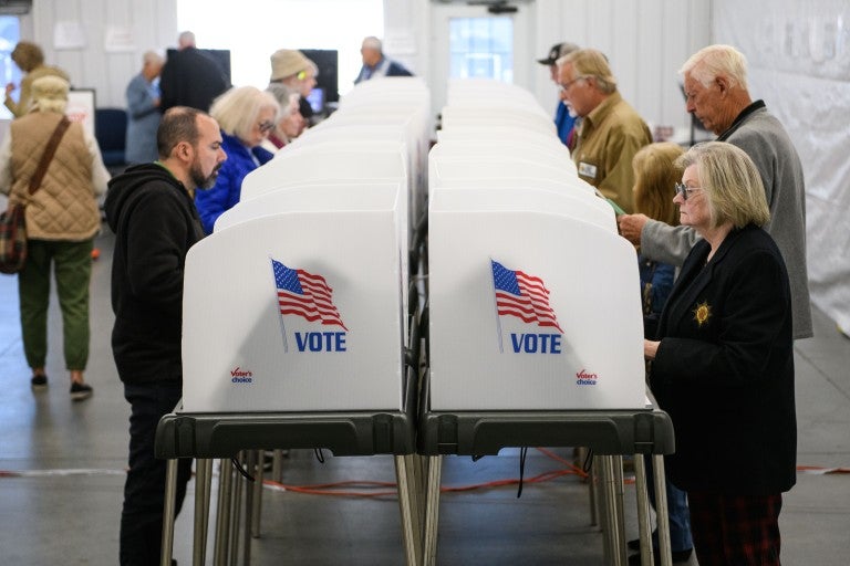 People standing on either side of white voting privacy booths with an American flag and the word "VOTE" stamped across the side