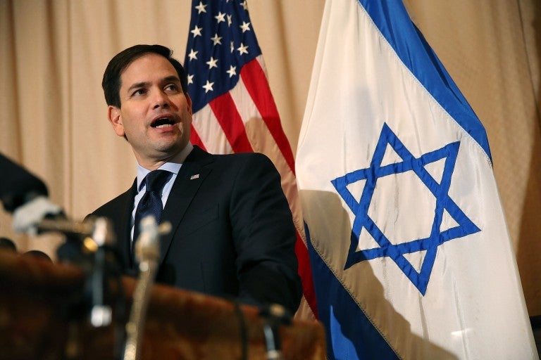 U.S. Sen. Marco Rubio (R-FL) speaks into a microphone, in front of U.S. and Israeli flags