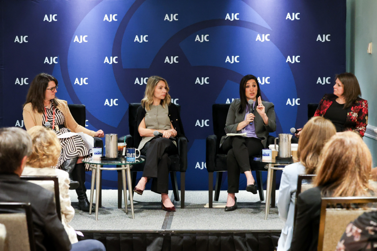 Four women sitting on in chairs on a stage, in front of a blue background with AJC logo. From left to right:  Manya Brachear Pashman, host of AJC's People of the Pod, AJC Casey Kustin, AJC’s Chief Impact and Operations Officer, former U.S. Deputy Assistant Secretary of State Mira Resnick, and Dana Stroul, Research Director and Kassen Family Senior Fellow at The Washington Institute for Near East Policy.