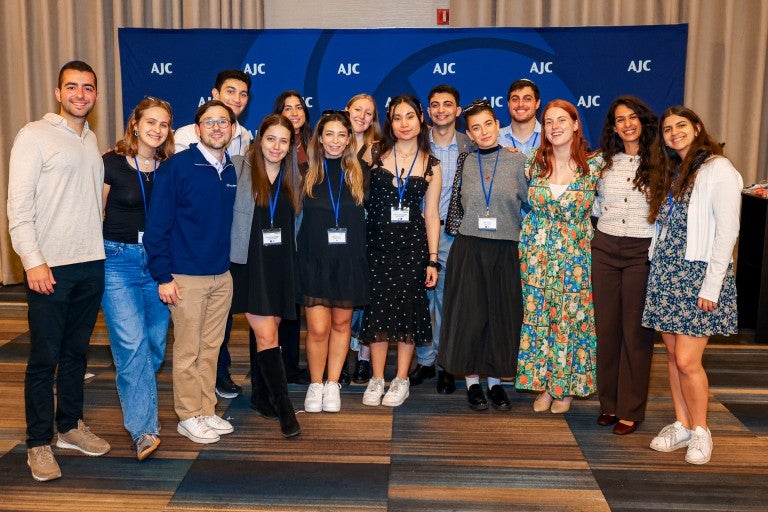 Jewish college students standing in front of an AJC blue background