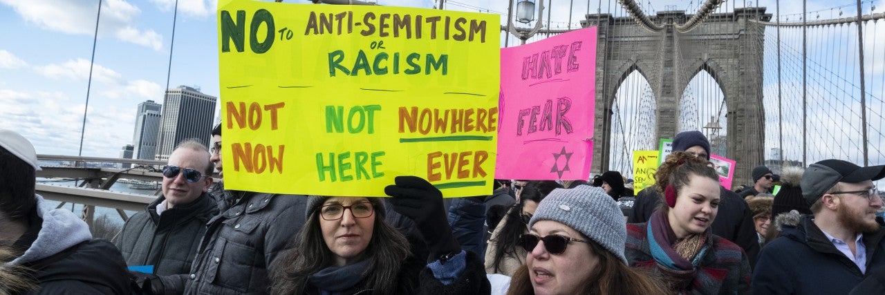 Photo of a woman at the No Hate march in NY holding a sign "No to Anti-Semitism or Racism -- Not now, Not here, Nowhere ever"