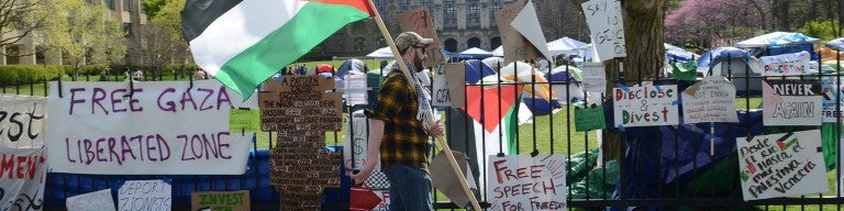 Encampment at Northwestern with signs and a student walking past with a Palestinian flag