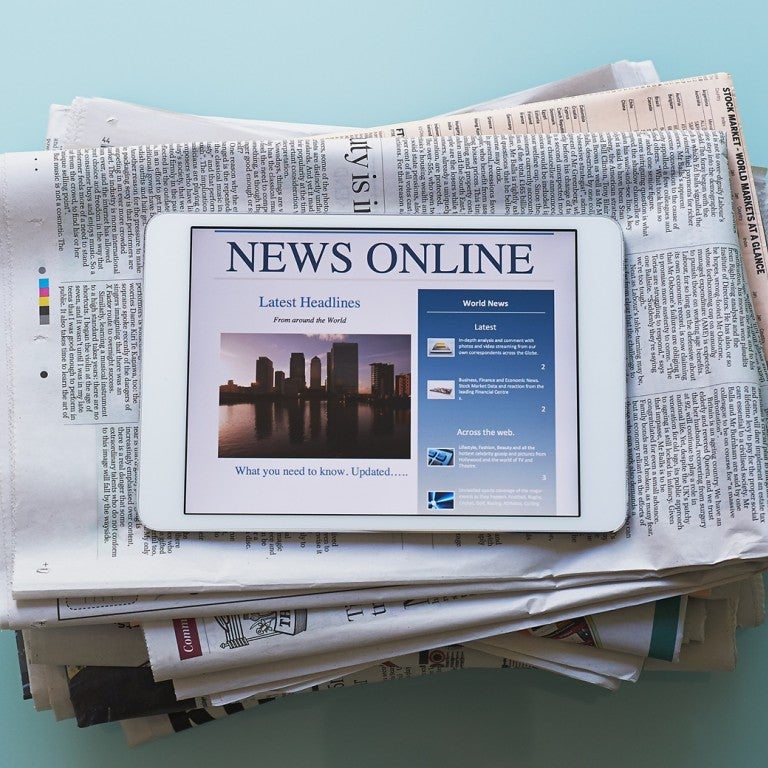 Photo of a stack of newspapers and an iPad displaying - News Online