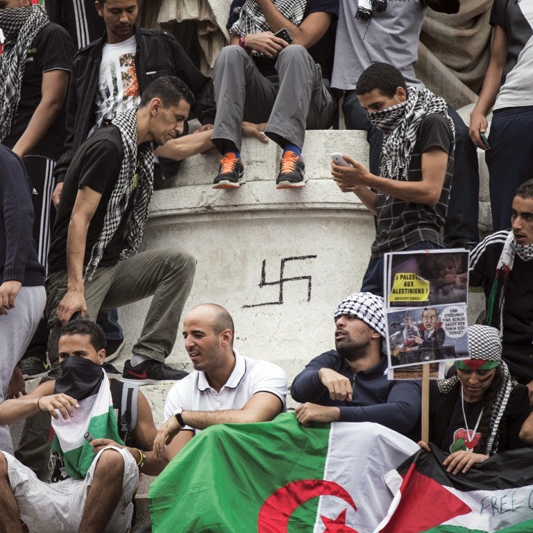 A group of extremist Muslims in Europe gathers around a statue with a swastika graffitted on it 