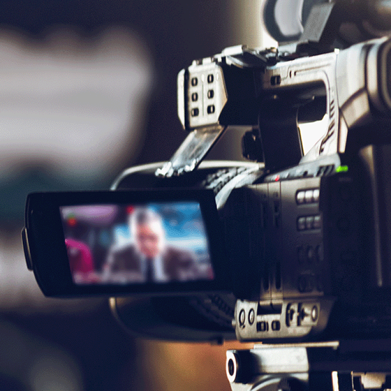 Photo of a video camera filming a news anchor