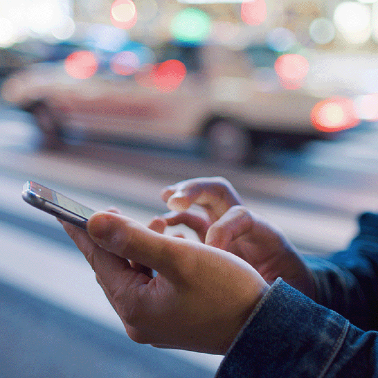 A photo of a person on their cell phone with a taxi in the background