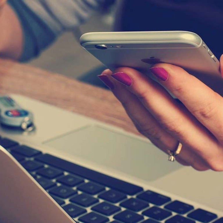 A woman holding a phone typing on her computer
