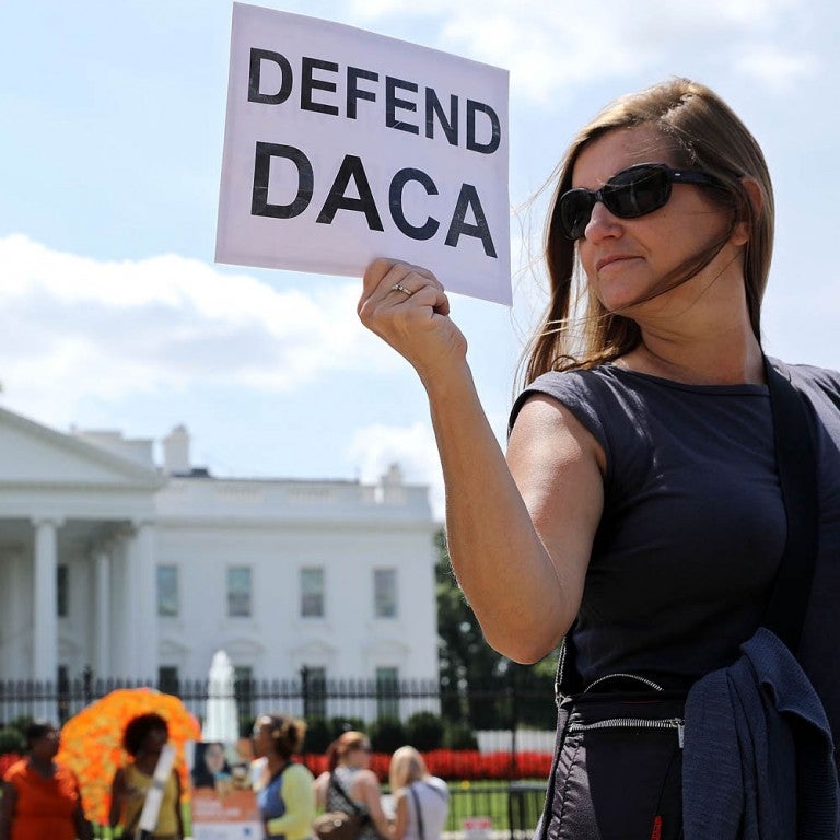 Photo of a woman holding a "Defend DACA" sign in front of the White House