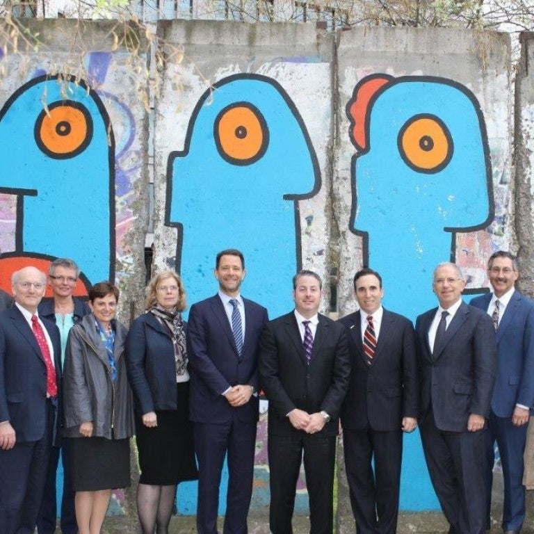 Photo of individuals on AJC-Adenauer Leadership Exchange Program standing in front of the Faces with Big Lips mural on a section of the Berlin Wall